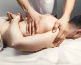 Masażysta wykonuje masaż tkanek głębokich pleców, skupiając się na mięśniach.
