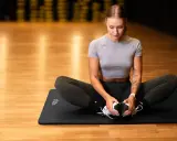 Kobieta w siłowni wykonuje ćwiczenie rozciągające na macie. Pilates co daje? Poprawia elastyczność i siłę.