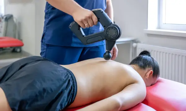 Fizjoterapeuta wykonuje masaż wibracyjny pleców. Choć zazwyczaj przynosi ulgę, warto pamiętać o potencjalnych skutkach ubocznych masażu wibracyjnego.